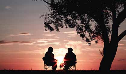 two people sitting in front of a sunset